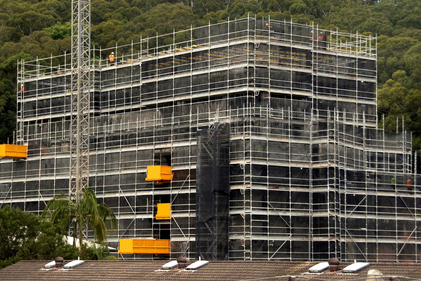 Industrial building fully encapsulated in sheeting behind scaffold and hoists